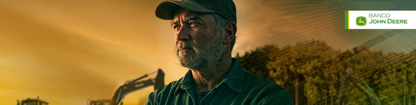 Um homem com os braços cruzados a frente de um campo com máquinas John Deere