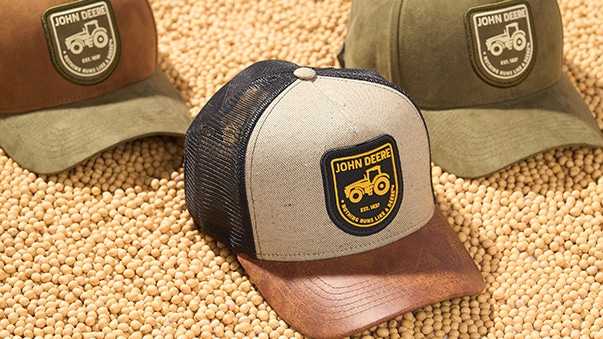 Três bonés da John Deere em cima de grãos.