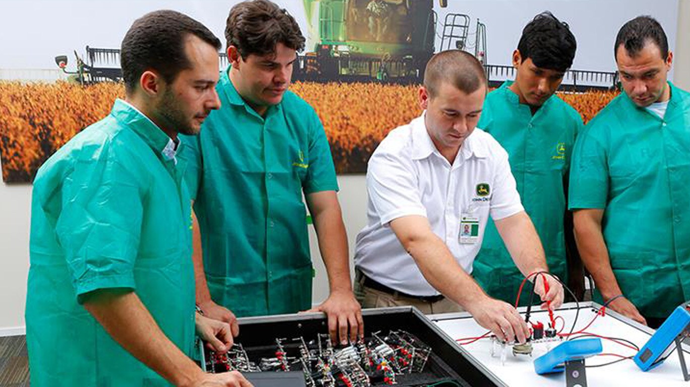 Pessoas em uma mesa com um instrutor de treinamento em uma instalação da John&nbsp;Deere