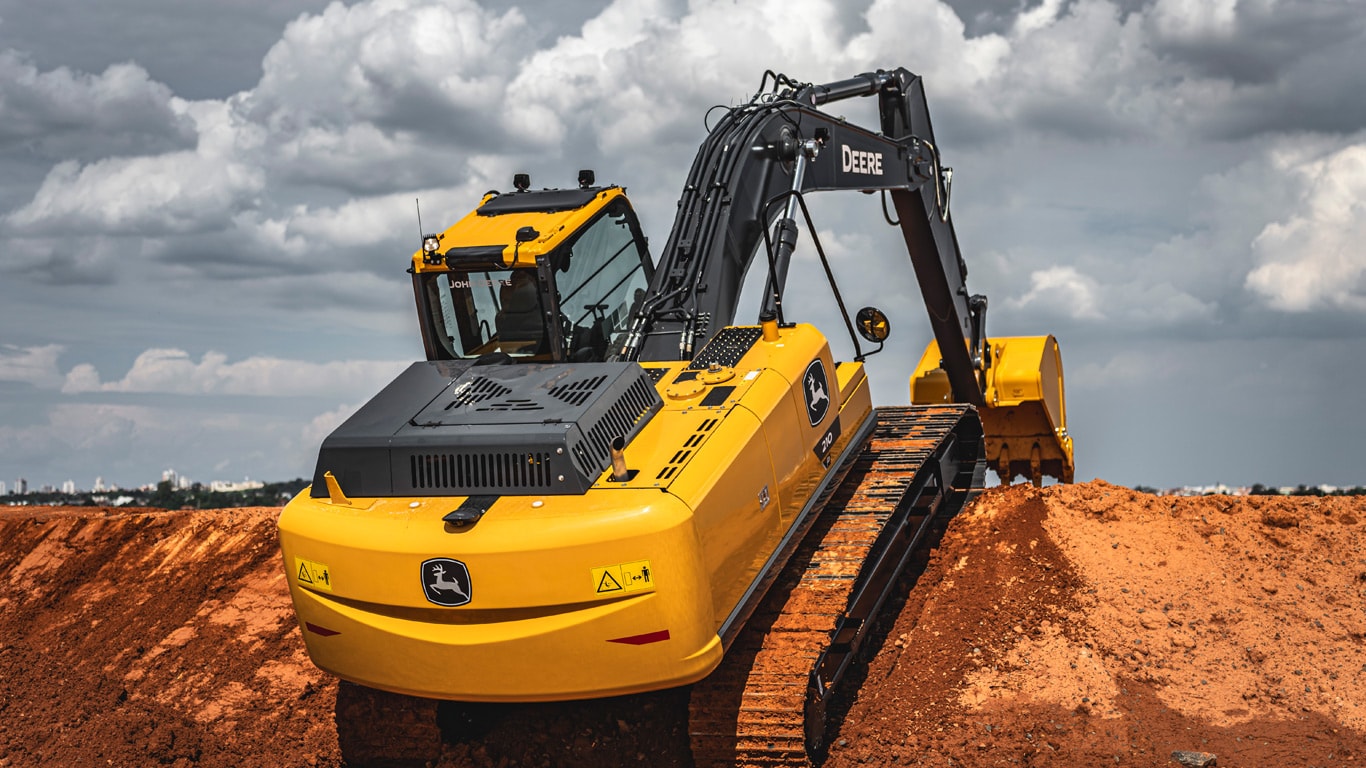 Escavadeira John Deere 210P amarela sobre terra em obra, sob céu nublado