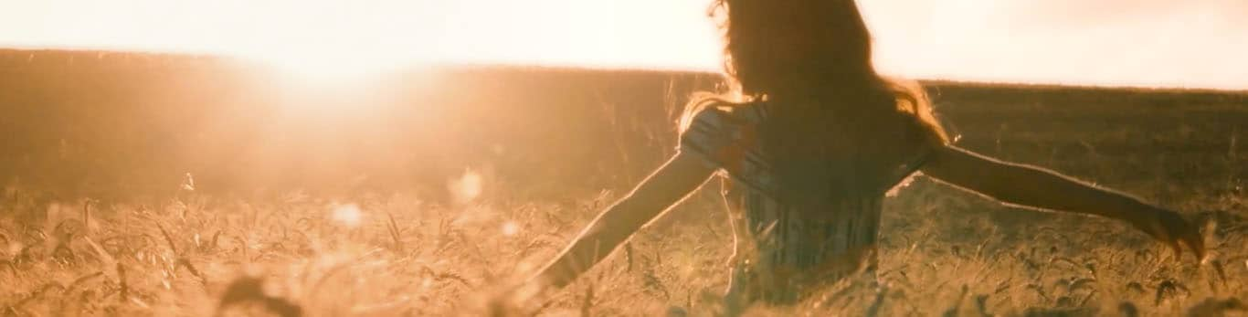 Menina andando com os braços abertos num campo de trigo.