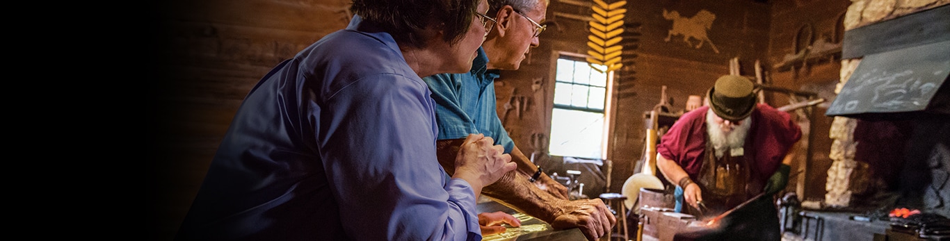Um casal idoso observa um ferreiro martelando um pedaço de metal no Local Histórico em Grand Detour, Illinois, Estados Unidos