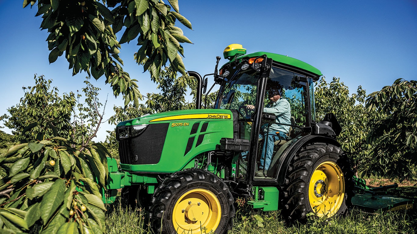 Um homem dirigindo um trator John&nbsp;Deere 5EN no campo.