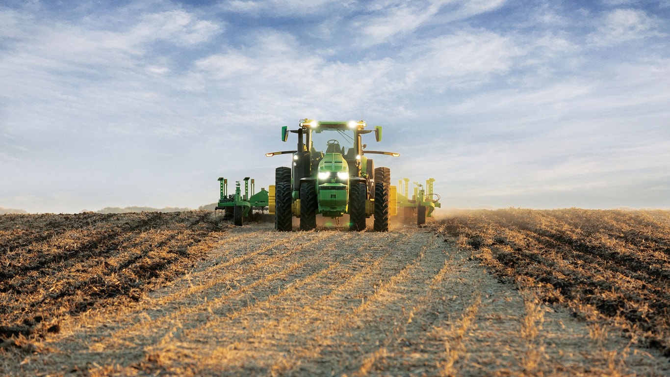 Trator John Deere autônomo puxando equipamento agrícola por um campo aberto.