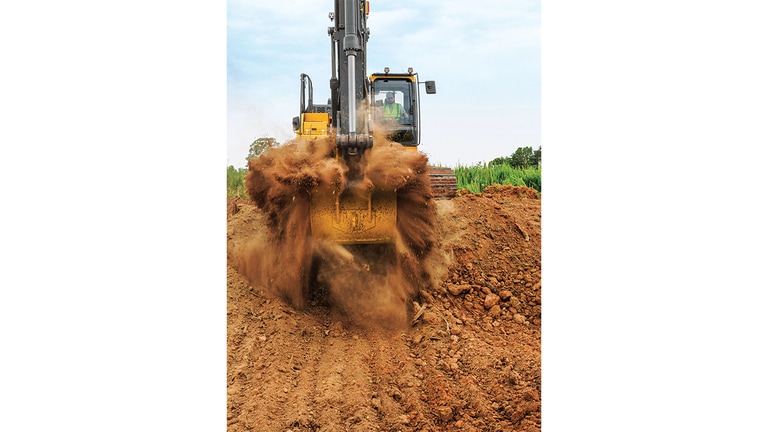 Uma perspectiva frontal de um operador removendo terra com uma Escavadeira Tier P 210 com um campo verde no fundo.