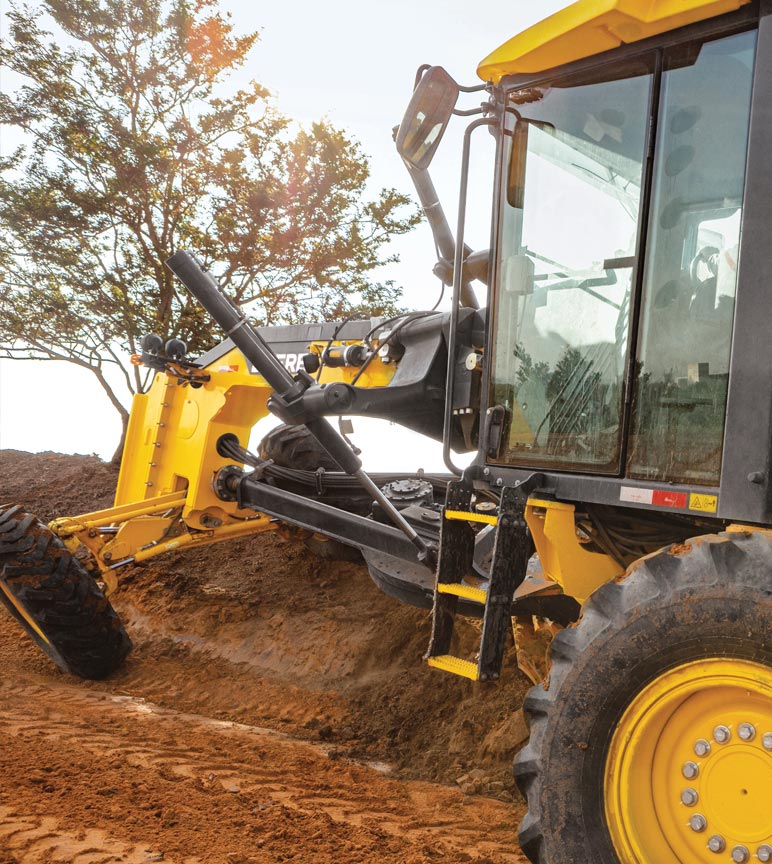 Veículo de construção amarelo cavando o solo com uma árvore no fundo.