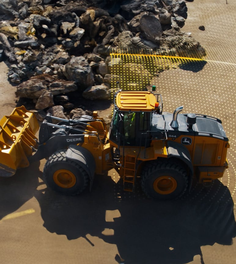 Uma pá-carregadeira de rodas grande e amarela John Deere 844 move pedras em um local de construção, com uma sobreposição de grade mostrando seu caminho.