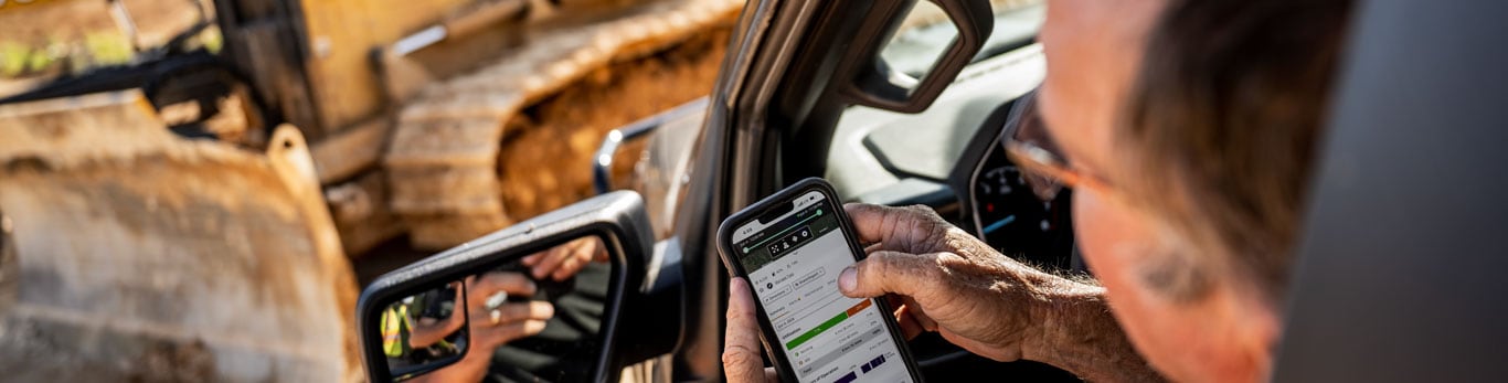 Um cliente da construção civil vê os dados da sua máquina em um celular.