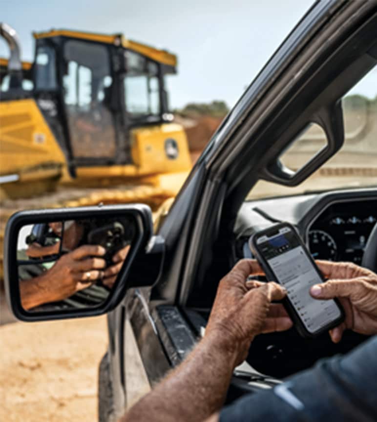 Trabalhador da construção civil em um caminhão interagindo com um telefone celular em um local de trabalho