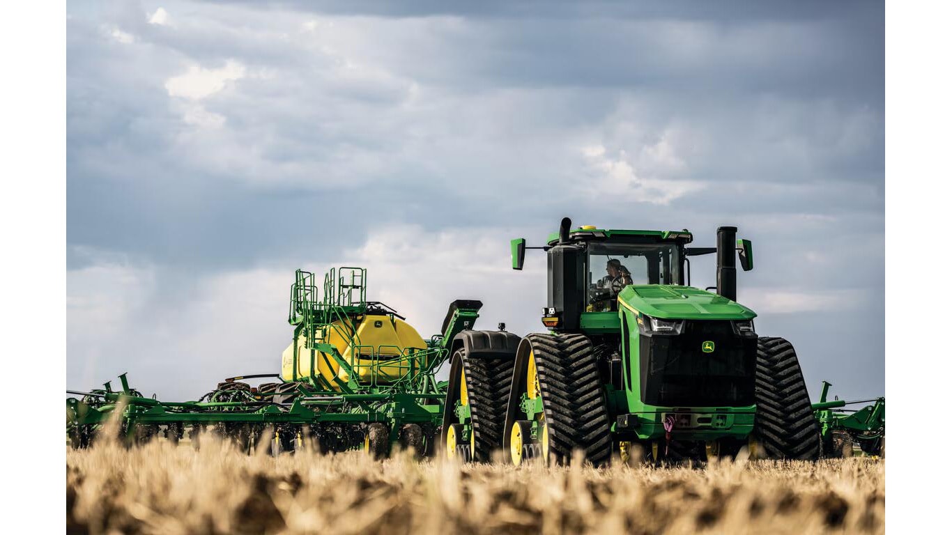 Trator em operação no campo, equipado com implemento agrícola de grande porte.