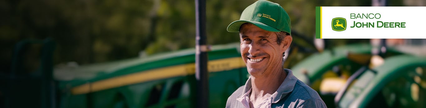 Homem sorrindo em frente a um trator da John Deere.