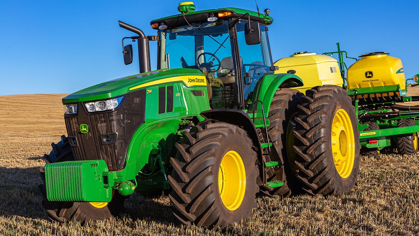 Trator 7m em um campo com céu azul e um implemento acoplado na traseira