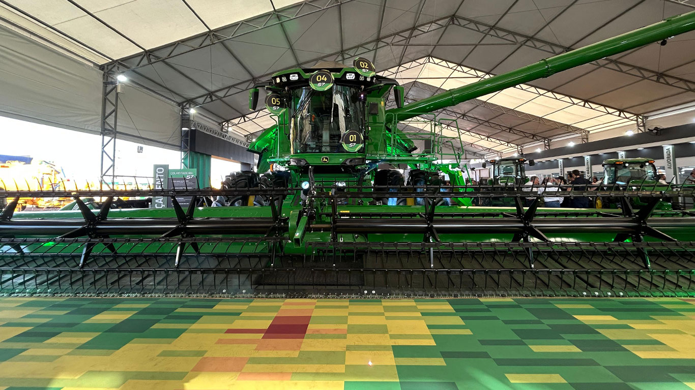 Imagem de uma grande máquina agrícola verde, colheitadeira S7, exposta sob uma tenda ampla.