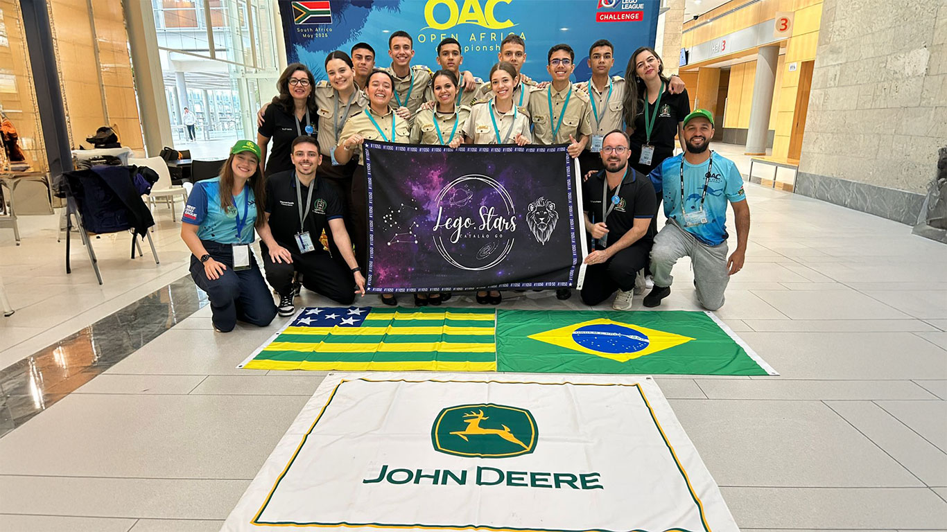 Grupo de jovens e adultos posa para foto em ambiente interno, sobre piso claro. Eles seguram um banner colorido com o nome “Lego Stars”