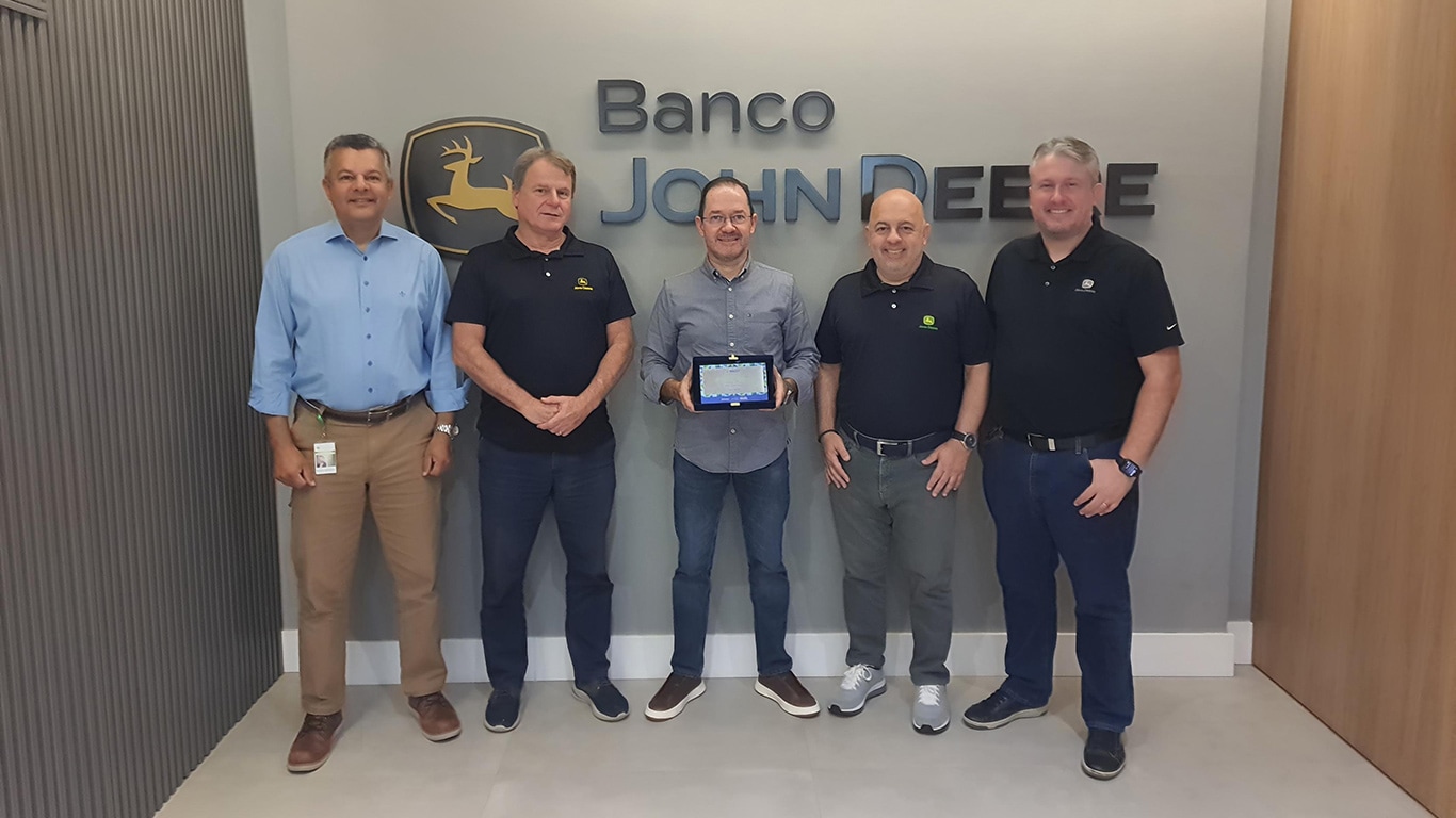 Foto em ambiente corporativo interno. Cinco executivos do Banco John Deere estão em pé, lado a lado, alinhadas de frente para a câmera.