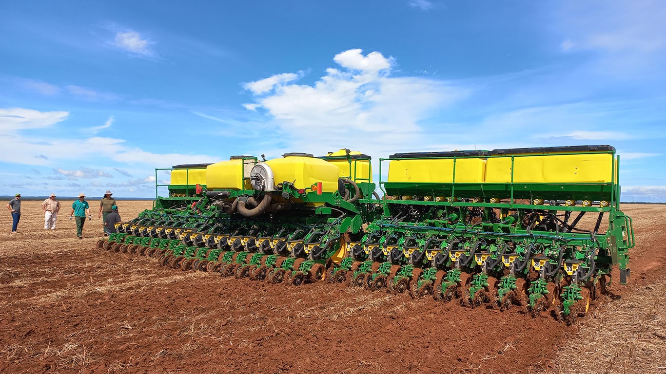 Plantadeira em um campo de terra arada com céu azul e pessoas por perto