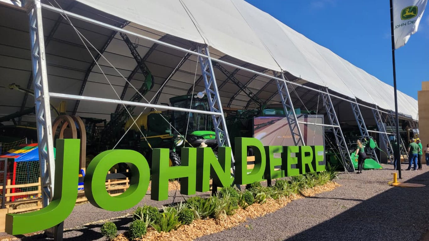 Estande da John Deere na Coopavel com letreiro verde e tenda exibindo máquinas.