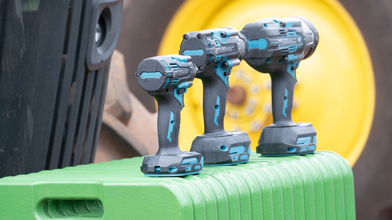 Tr&ecirc;s ferramentas el&eacute;tricas sem fio alinhadas, em cinza‑escuro com detalhes azul‑claro.