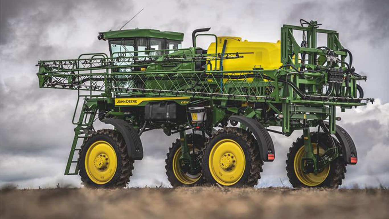 Pulverizador 1025E verde com tanque amarelo e barras dobradas sob céu nublado.