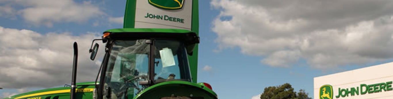 Topo de um trator John Deere na frente de um concessionário.