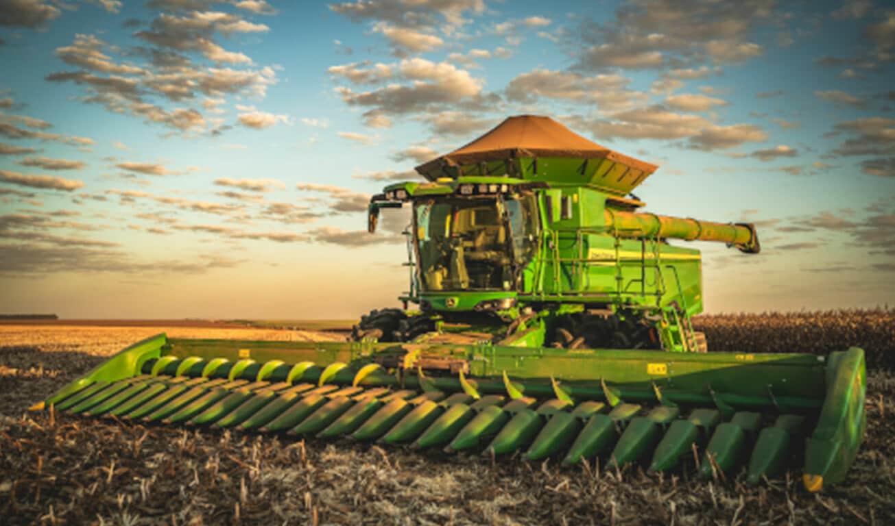 Colheitadeira verde equipada com plataforma de milho em campo colhido ao entardecer.