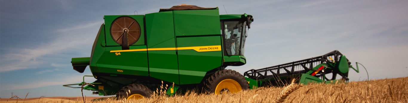 A colheitadeira John Deere S4 colhe gr&atilde;os em um campo sob c&eacute;u aberto.