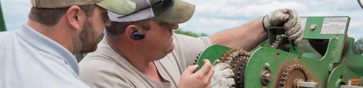 Dois homens consertando um trator John Deere