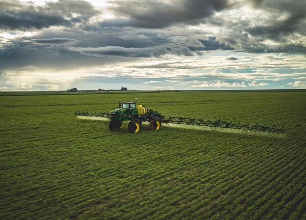 Pulverizador agrícola aplicando insumos em campo verde sob céu nublado.