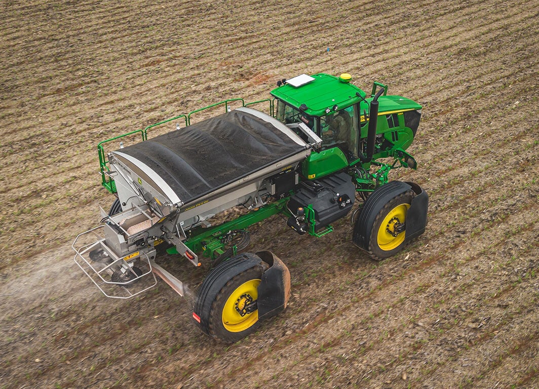 Distribuidor agrícola autopropelido visto de cima aplicando insumos em campo seco.