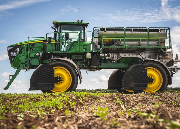 Pulverizador agrícola autopropelido em perfil lateral sobre plantação jovem.