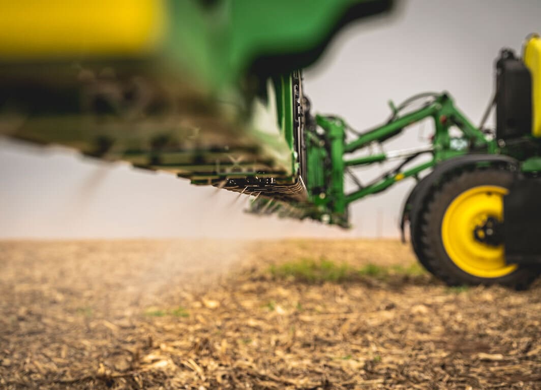 Detalhe da barra de pulverização agrícola em funcionamento sobre solo seco.