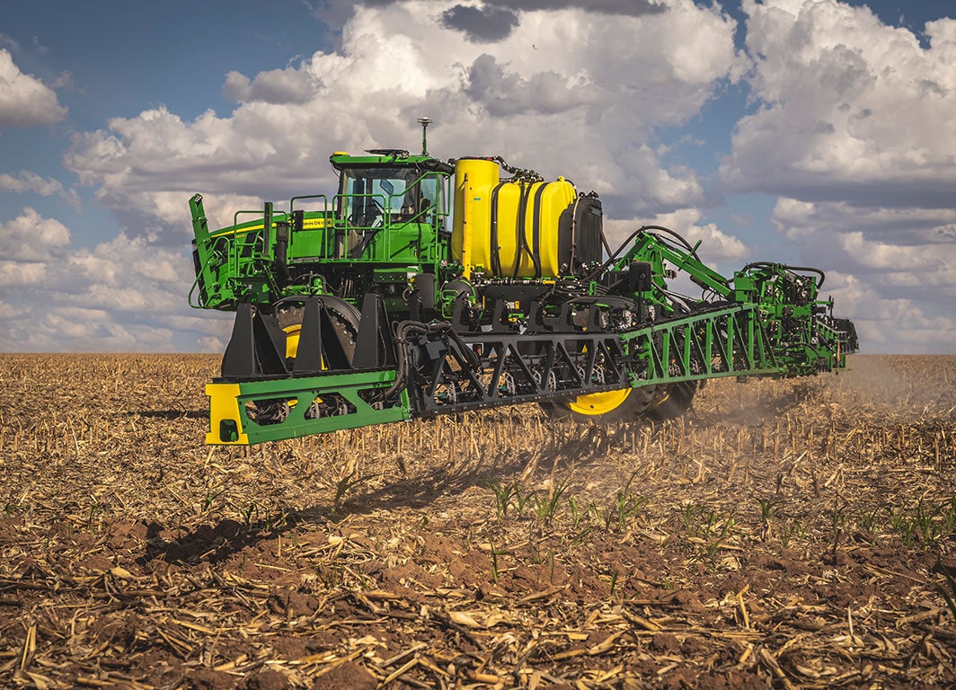 Pulverizador agrícola autopropelido com barras abertas em campo sob céu nublado.