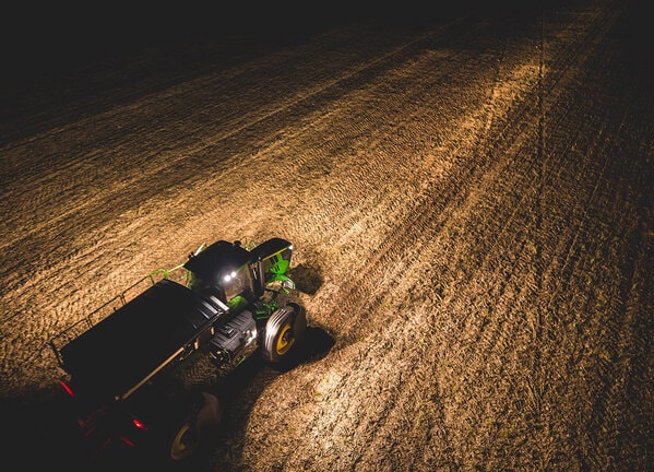 Distribuidor agrícola operando à noite com luzes acesas em lavoura.