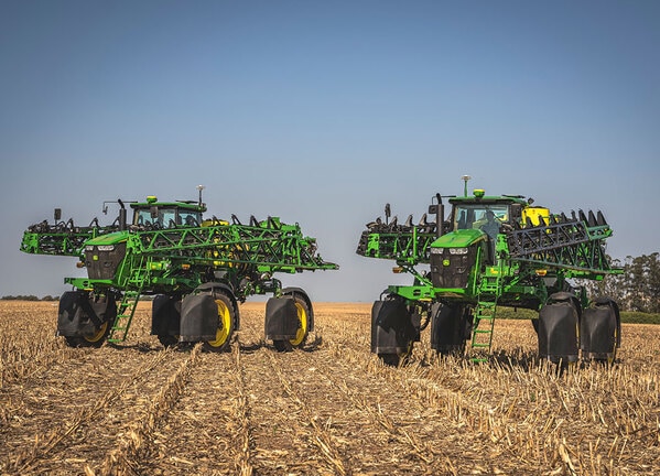 Dois pulverizadores agrícolas autopropelidos posicionados em campo colhido.