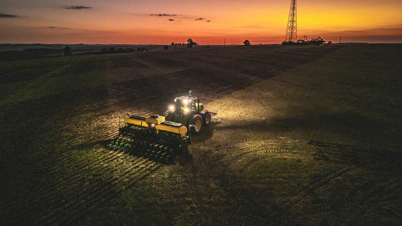 Vista aérea de um trator 1207 com uma plantadeira trabalhando em um campo ao anoitecer