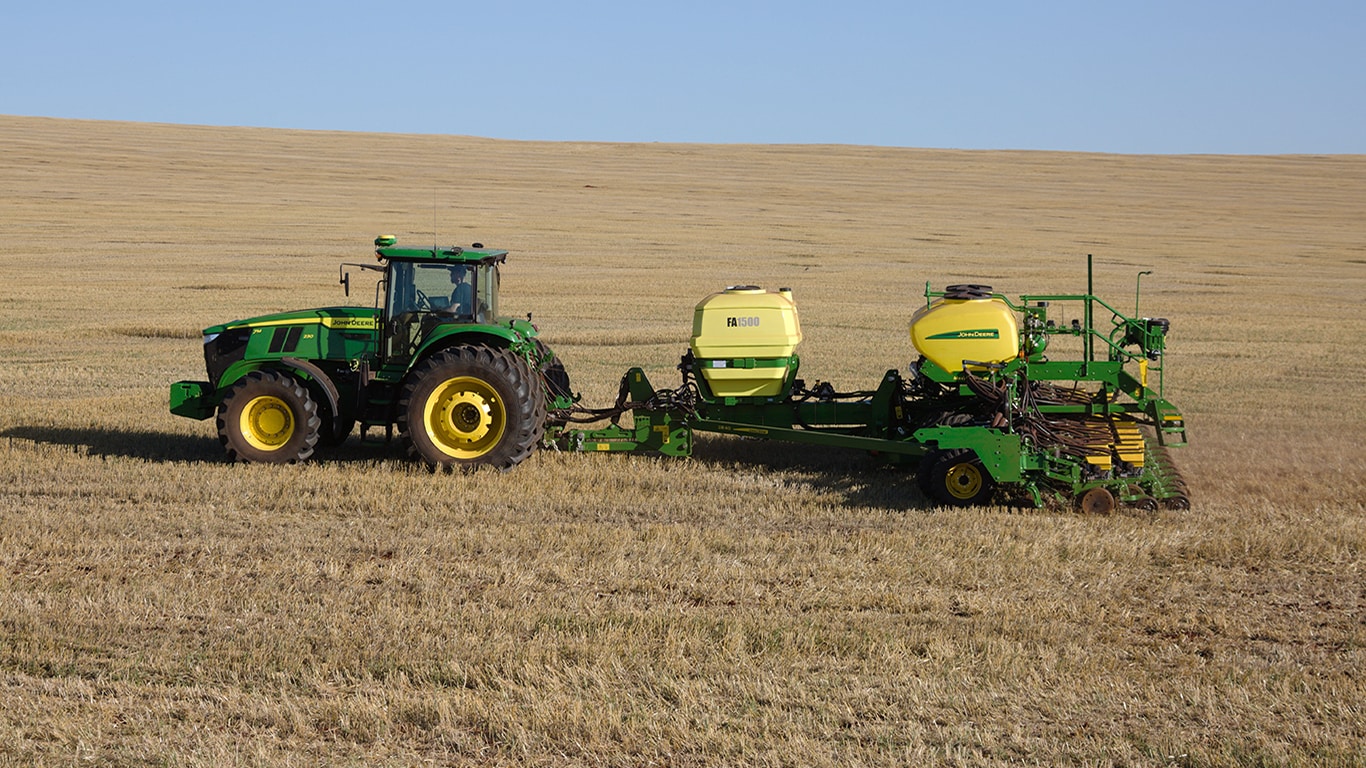 Plantadeira John Deere, com um tanque inoculante, sendo puxada por um trator John Deere em um campo aberto.