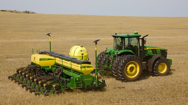 Plantadeira John Deere, com um tanque inoculante, sendo puxada por um trator John Deere em um campo aberto.