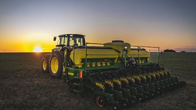 Máquina John Deere série 1200 no campo ao entardecer.