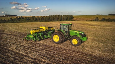 Máquina John Deere série 1200 no campo ao entardecer.