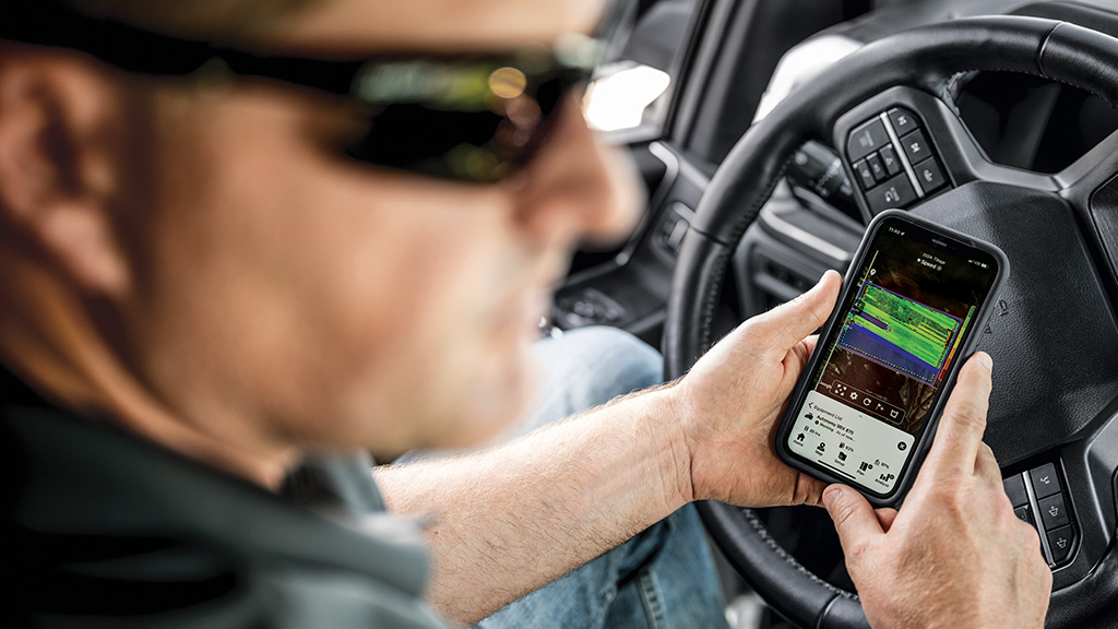 Homem dentro de uma cabine olhando no celular um mapa de dados agrícolas com informações da operação em campo.