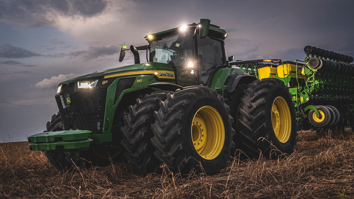 Trator 8R540 John Deere no campo a noite.