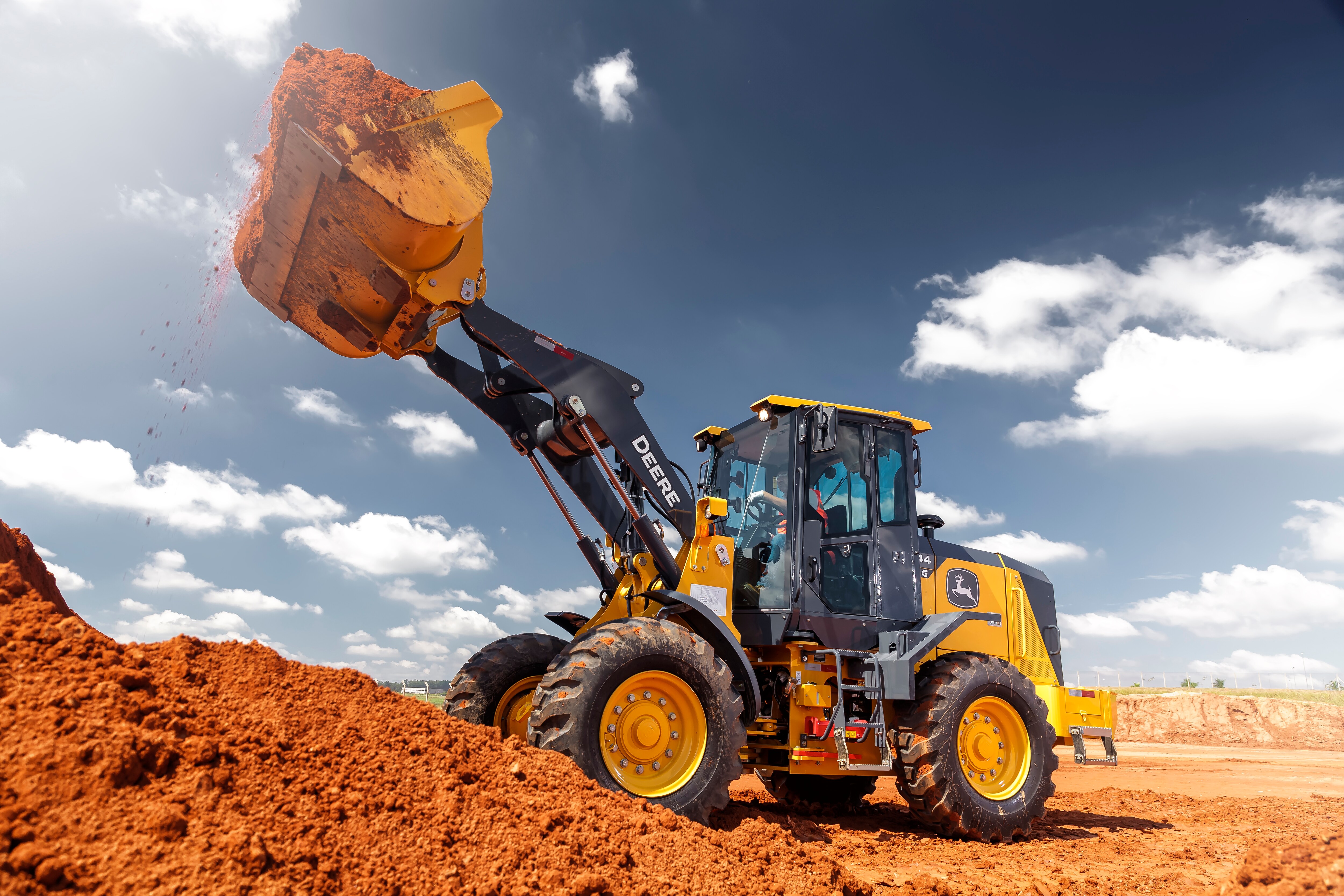 Pá Carregadeira 444G em campo com a caçamba levantada carregando terra